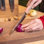 Sakai kyuba santoku blue cutting an onion on walnut cutting board