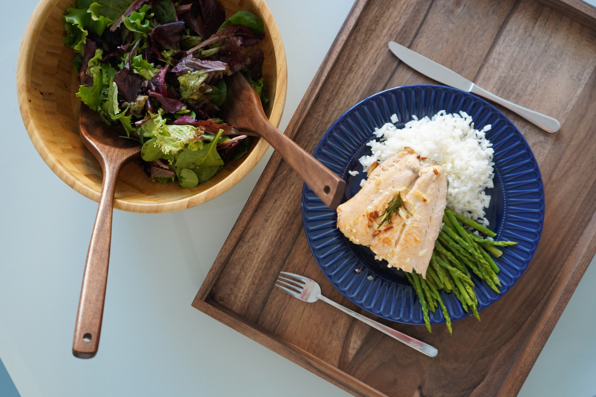 Cooked salmon and salad on wooden tray and dark walnut utensils