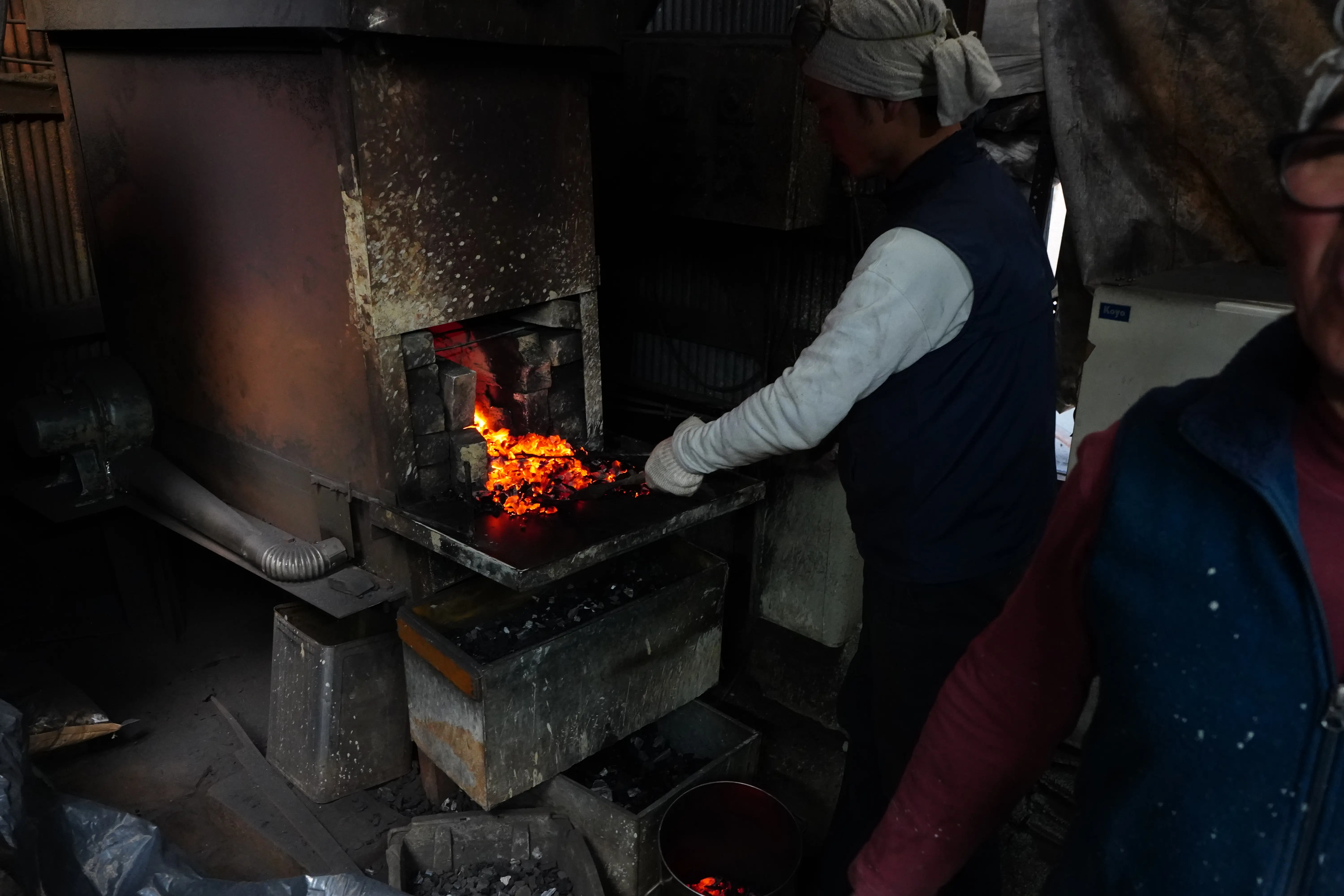 A blacksmith in a headscarf working the forge fire